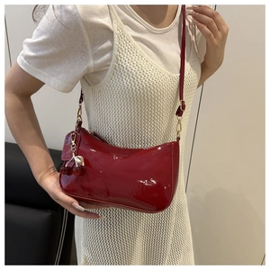 Détail d'un sac baguette en cuir verni rouge foncé avec un charmant pendentif cerise