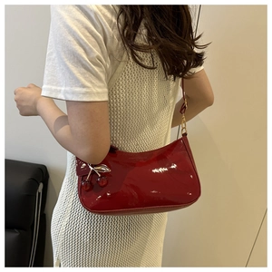 Detailed view of red glossy patent leather underarm bag with cute cherry pendant
