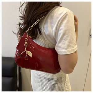 Detail of red patent leather underarm bag featuring a cherry charm and metal chain