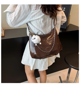 Détail du sac hobo marron foncé brillant avec chaîne argentée et pompon blanc en peluche