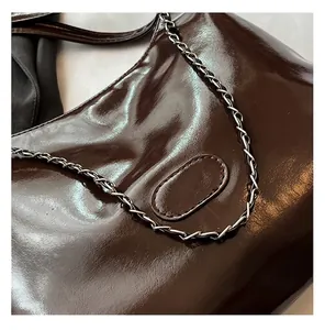 Gros plan sur un sac cabas en cuir verni marron foncé avec chaîne et surpiqûres