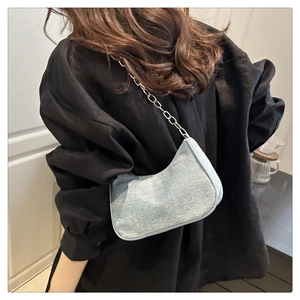 Détail du sac croissant bleu clair avec chaîne argentée porté sur une chemise noire