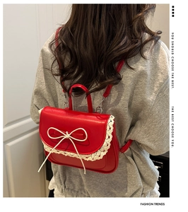 Detail of red leather mini backpack featuring white lace trim and bow on the back of model