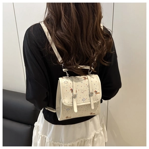 Detail eines cremefarbenen Mini-Rucksacks mit Dackel-Print und Cartoon-Mustern am Modell