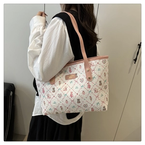 On-shoulder view of a large white tote bag with pink cartoon bear prints and straps