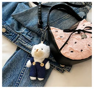 Detail of white plush bear pendant with denim overalls on a stylish handbag