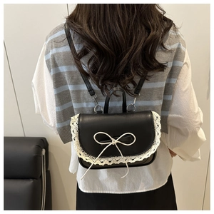 Detail of mini black backpack with white lace edges and bow on a model's back