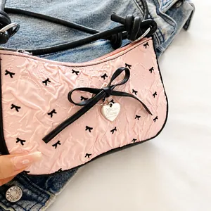 Detail of pink crescent bag with black bow prints and heart pendant on denim texture