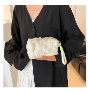 Detail of plush off-white makeup bag with fleece texture and green woven accents