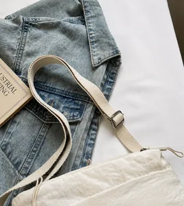Detail of adjustable gray textile shoulder strap and metal buckle on cream crossbody bag