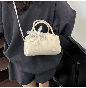 Détail du sac Boston crème avec chaîne de perles et nœud en dentelle sur bandoulière