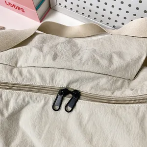 Dettaglio della doppia cerniera e della trama in nylon sulla borsa a tracolla beige