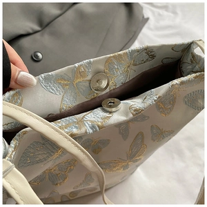 Close-up of magnetic clasp and delicate butterfly embroidery on a beige bucket bag