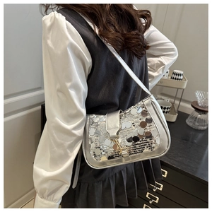 Détail du sac à bandoulière à paillettes argentées avec boucle dorée porté par un mannequin