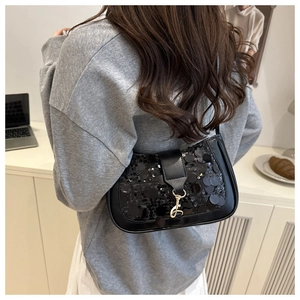 Detail of black sequined shoulder bag with golden metal clasp on a model in daily setting