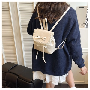 Nahaufnahme eines Mini-Rucksacks in Creme mit Spitzenbesatz und Schleife am Rücken