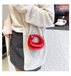Glossy red moon-shaped mini bag with gold chain strap shown on a model's outfit
