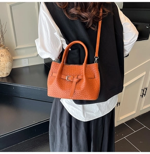 Close-up of orange woven bucket bag styled on a model in a modern interior setting