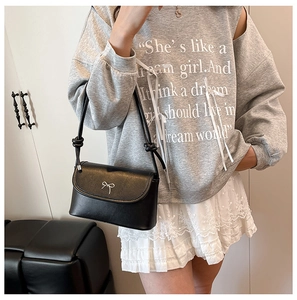 Détail d'un sac bandoulière en cuir noir avec un nœud en métal argenté et sangle à nœuds