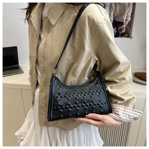 Detailed view of black quilted baguette bag with chic diamond pattern on model shoulder