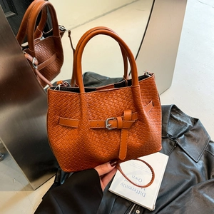 Brown woven leather bucket bag with metal buckle and shoulder strap in lifestyle setting