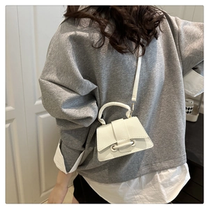 Detail of white mini crossbody bag with litchi texture and asymmetric trapezoid shape