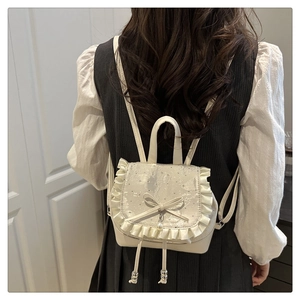 Close-up of white mini backpack with ruffle edges, bow detail, and pearl pendant accent