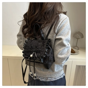 Detail of black bow backpack featuring ruffle trim and pearl pendant on a female model