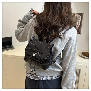Detail of black bow backpack featuring polka dot fabric and pearl pendant on a model