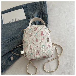 Detail of white quilted mini backpack with cartoon prints and metal chain strap