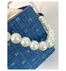 Detail of denim crossbody bag with star embroidery and white pearl chain handle