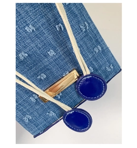 Macro shot of blue denim bag featuring white woven drawstrings and gold metal hardware