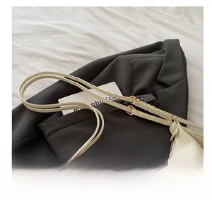 Detail of off-white faux leather shoulder bag with gold buckles and dual adjustable straps