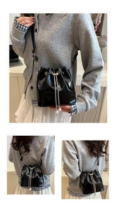 Detail of black drawstring bucket bag featuring silver chains and elegant pearl pendants
