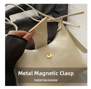 Detail showing the golden metal magnetic buckle and smooth cream PU leather of the handbag