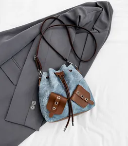 Detail of blue denim bucket bag with brown leather trim leaning on a grey blazer