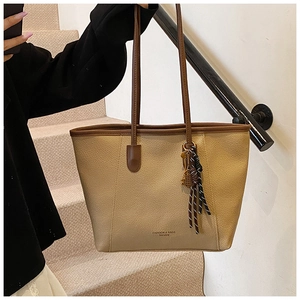 Dettaglio della borsa tote beige con manici marroni, pelle martellata e ciondolo tennis