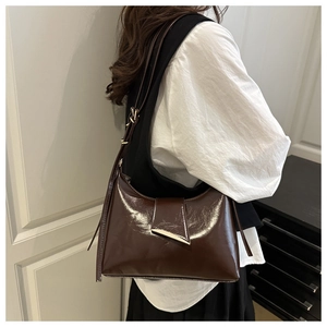 Gros plan du sac sous le bras en cuir verni marron avec boucle en métal doré