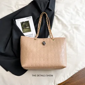 Detail of beige tote bag with embossed skull pattern and metallic skull buckle