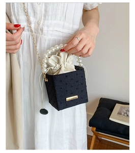 Detail of black fabric bucket bag with pearl handle and gold chain strap on white dress