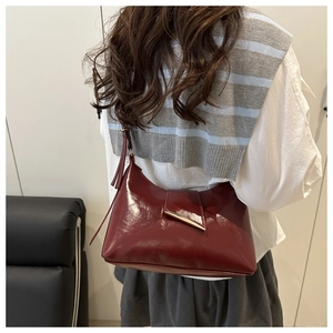Detail of burgundy glossy shoulder bag with gold metal buckle shown on a model shoulder