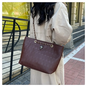 Close-up of brown leather tote bag with skull embossing and gold chain strap detail
