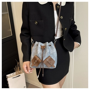 Détail du sac seau en denim bleu avec garniture en cuir marron et œillets métalliques