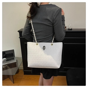 Detail of white tote bag with embossed skulls and silver skull metallic hardware
