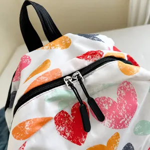 Close-up of smooth black zippers and colorful heart pattern on white canvas backpack