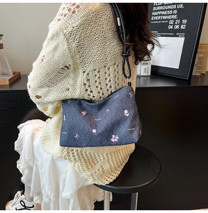 Close-up of a blue denim shoulder bag with pink floral embroidery and knot detail