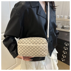 Detail of trendy beige crossbody bag featuring grey M-pattern print and slim shoulder strap