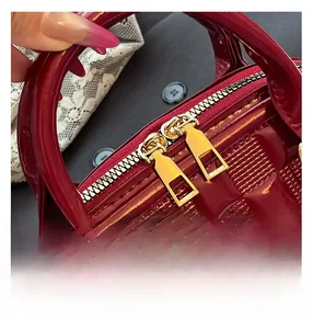 Detail of red patent leather handbag showing square embossing and gold zippers