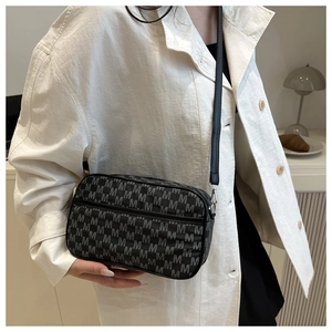 Detail of black crossbody camera bag with silver M pattern and adjustable strap on model