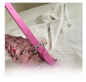 Detail of adjustable metal buckle on a pink sequin shoulder bag with leather strap